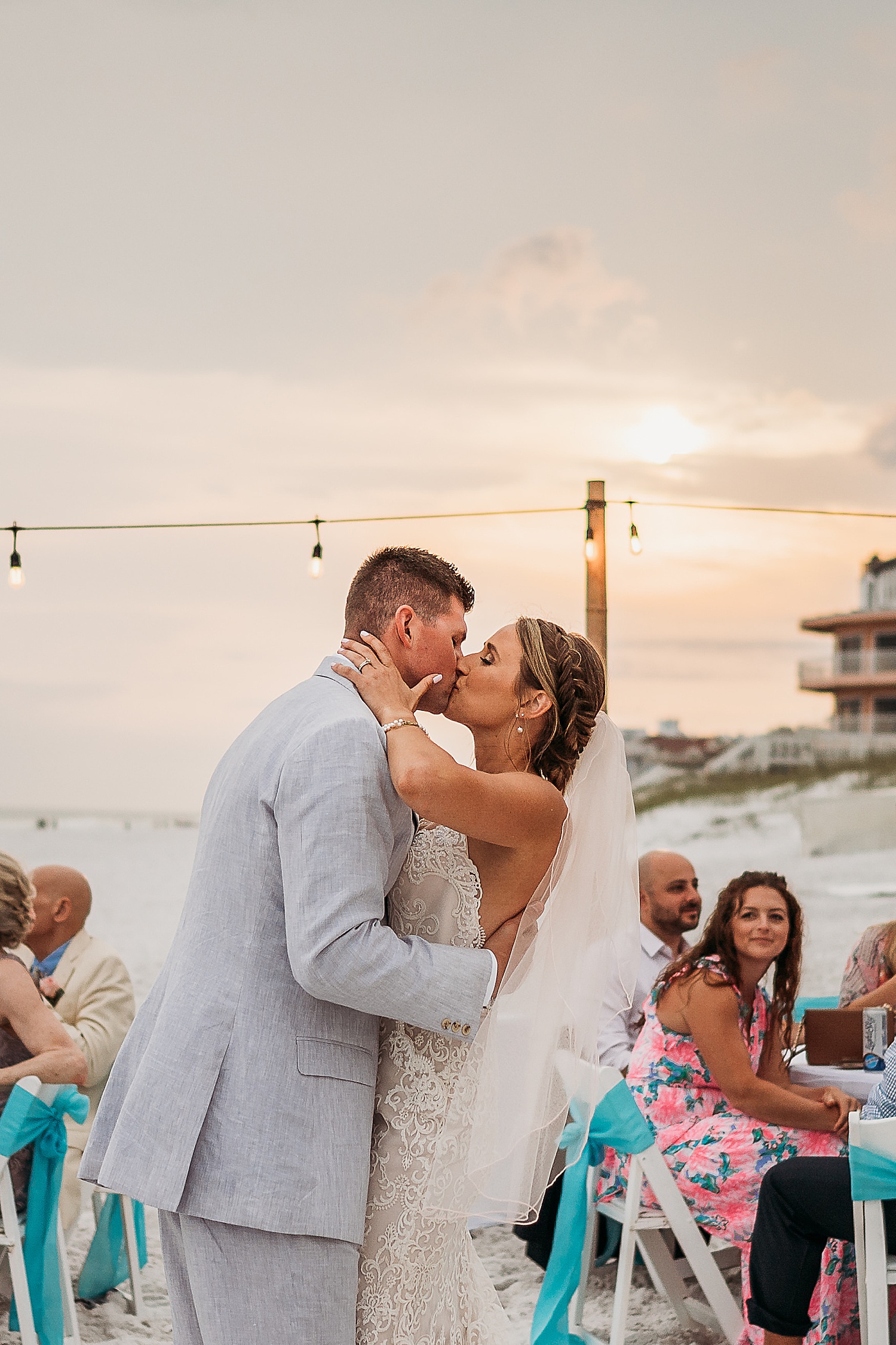 kissing at sunset in front of friends and family at wedding reception wearing veil in hair 