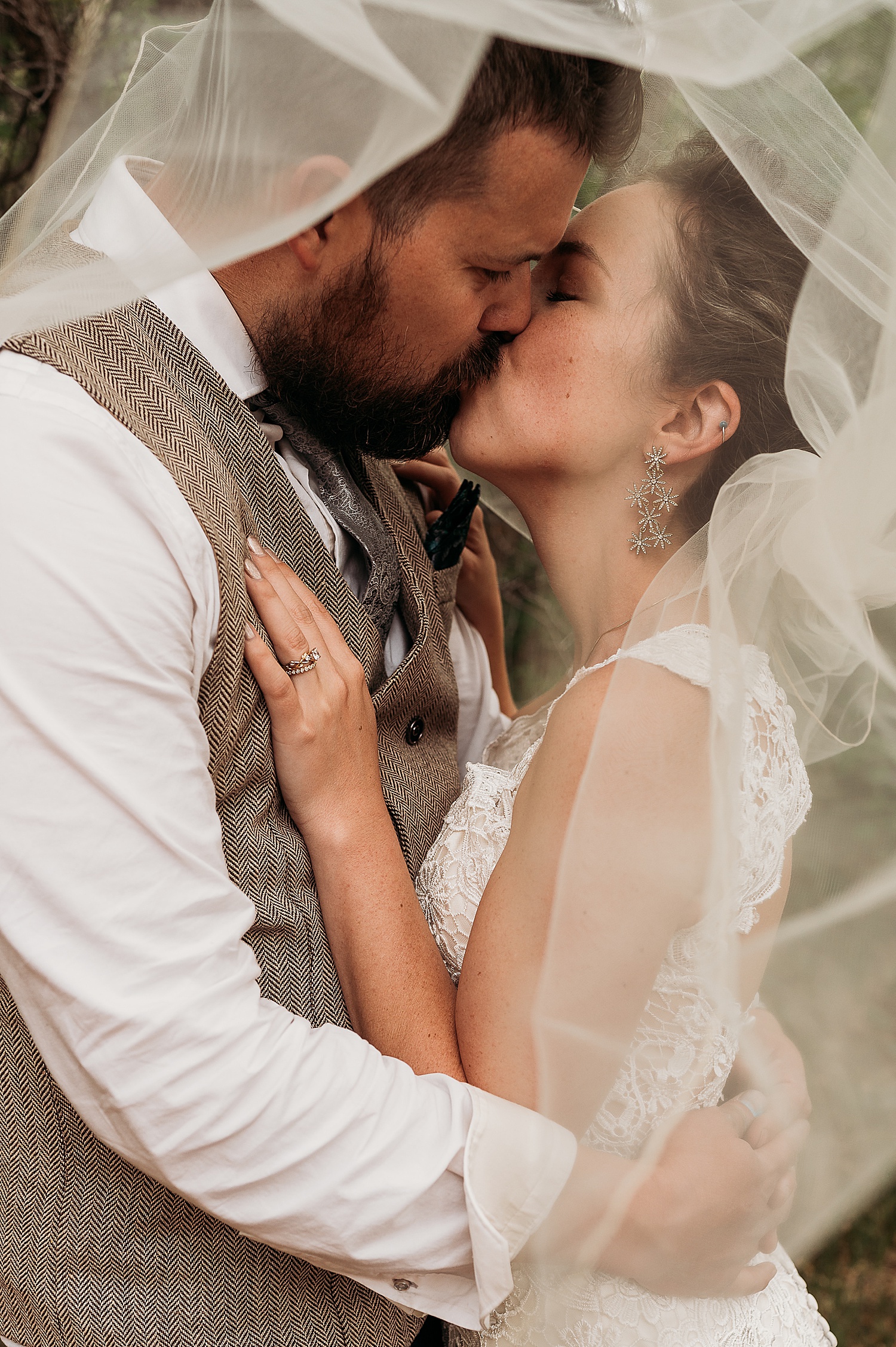 bride wears long veil and long earrings on wedding day while kissing new husband 