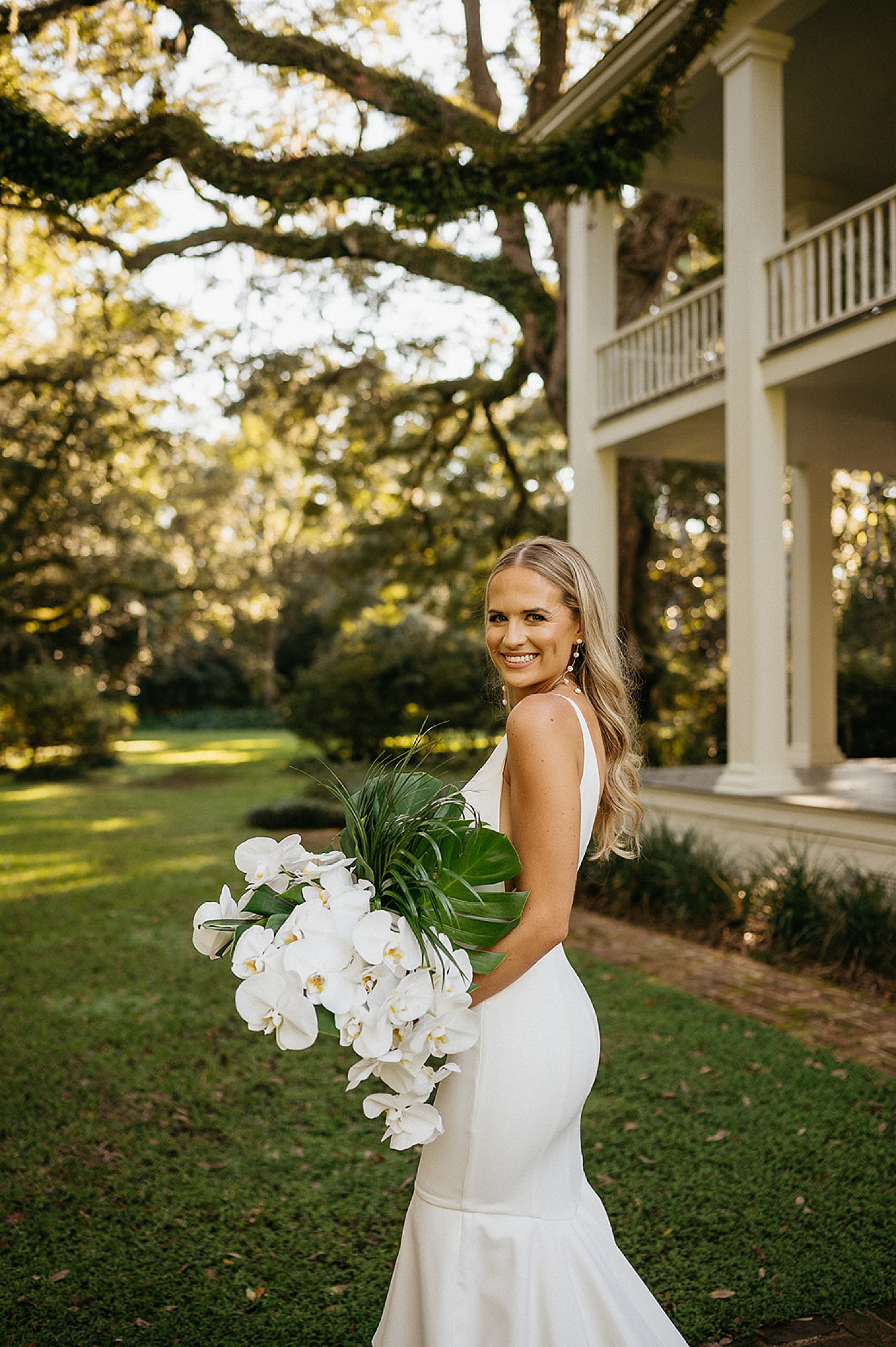 Bride wearing wedding dress holding white and green bouquet with orchids and palm leaves 