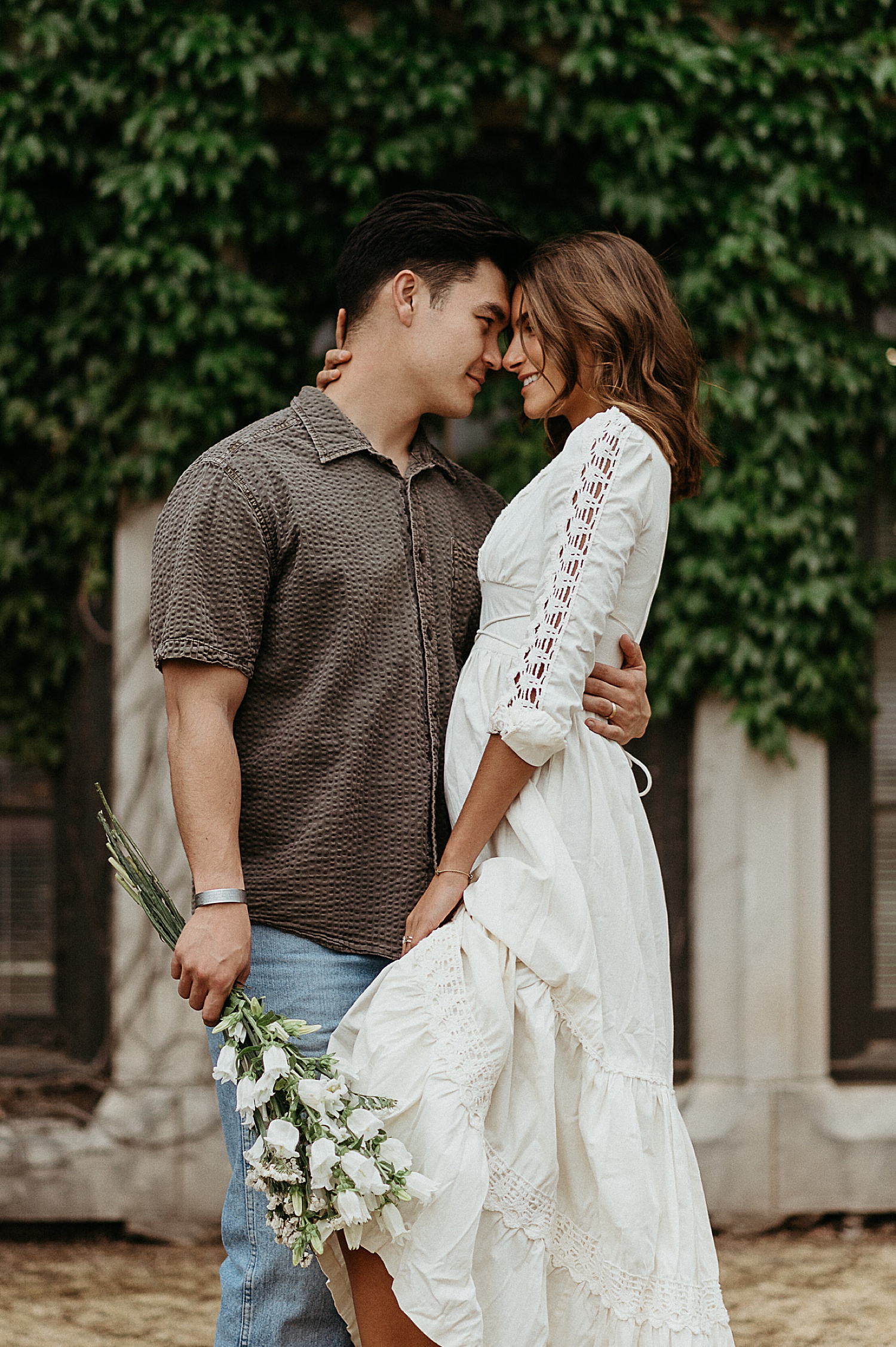 woman wearing long white dress while holding rose florals during city couples session 