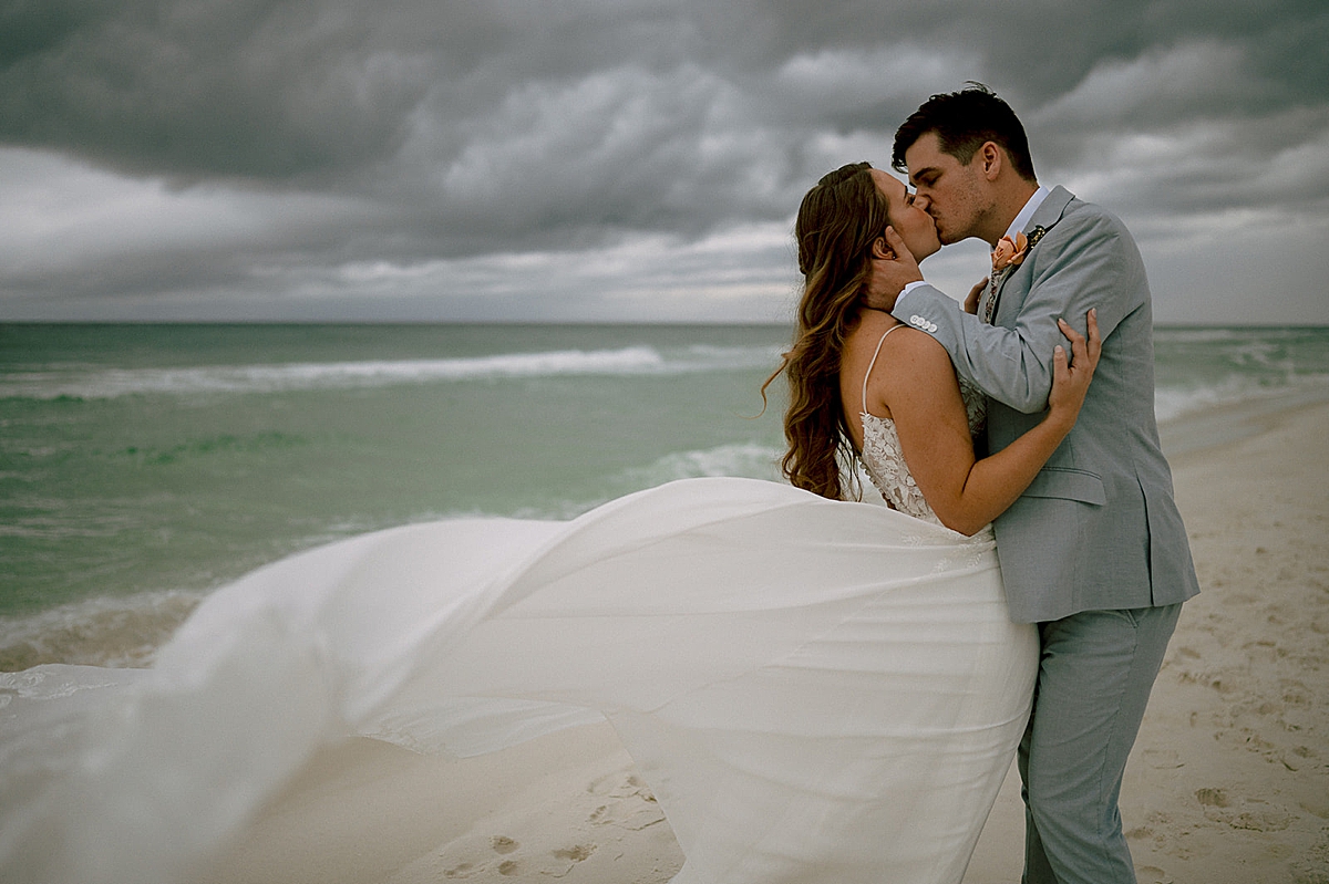 wedding dress train photo of newly married couple kissing on the beach by destination wedding photographer 